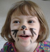 A little girl with black whiskers and a cat's nose painted on her face.