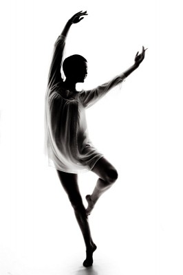 A dancer, her face and form eclipsed by shadow, arcs her body