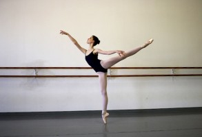 IMAGE A ballet dancer in leotard and tights poses in arabesque inside a dance studio. IMAGE