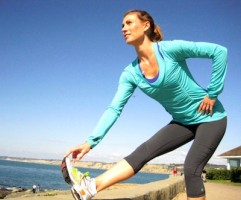 IMAGE A woman stretches her hamstring with one leg up on a low wall by the sea. IMAGE