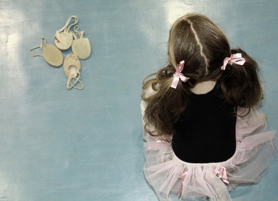 ballerina-child-dreaming IMAGE A young ballerina sits on a blue floor near a group of ballet slippers IMAGE