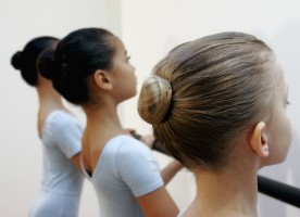Three young dancers stand at the barre, their tiny hair buns perfectly poised on their heads.