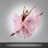 A ballerina bursts into a leap framed by her large pink skirt and a halo of light.