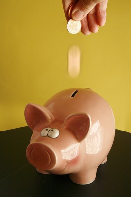A photo of someone dropping coins into a piggy bank