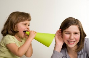 A little girl uses a megaphone to tell a secret to another