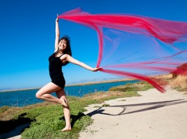 [image] A dancer stands on a beach, posing on one leg with a long scarf extended in the breeze. [image]