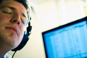 IMAGE A man listens to music through headphones with his eyes closed. A computer screen is in the background. IMAGE