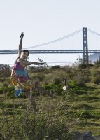 IMAGE A lone dancer in a colorful dress dances in a field with San Fancisco's Golden Gate Bridge in the background. IMAGE