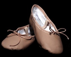 IMAGE Empty pair of child's ballet shoes displayed against a black background. IMAGE