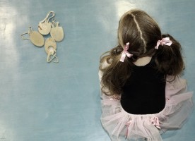 IMAGE A young ballerina sits on a blue floor near a group of ballet slippers IMAGE