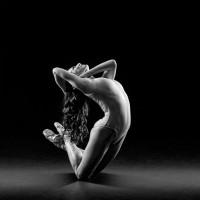 A dancer in shadow and light arches, looking upward while poised on her knees